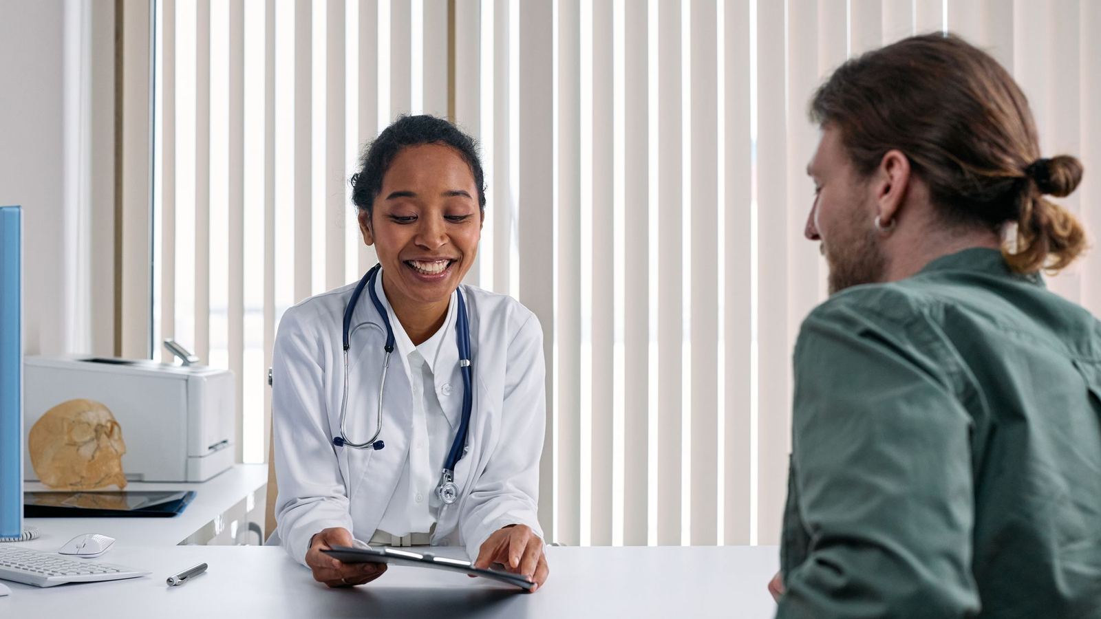 Doctor smiling while talking with a patient beside a bright window in a clinic