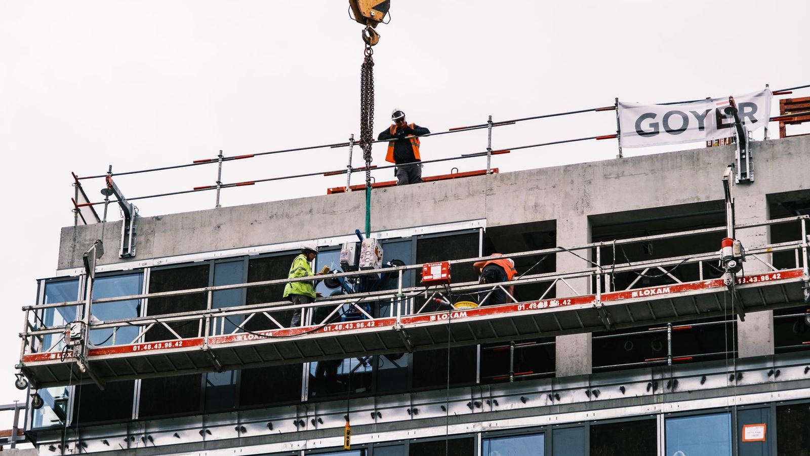 Construction workers on a suspended platform installing glass panels on a building