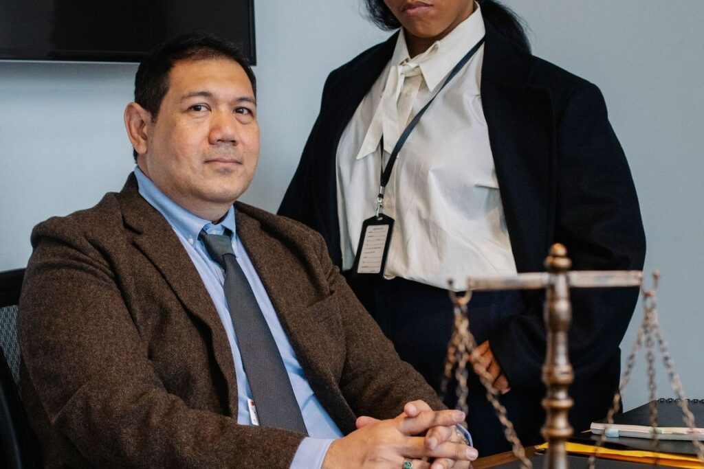 Attorney seated at his desk with a colleague standing behind him in a law office